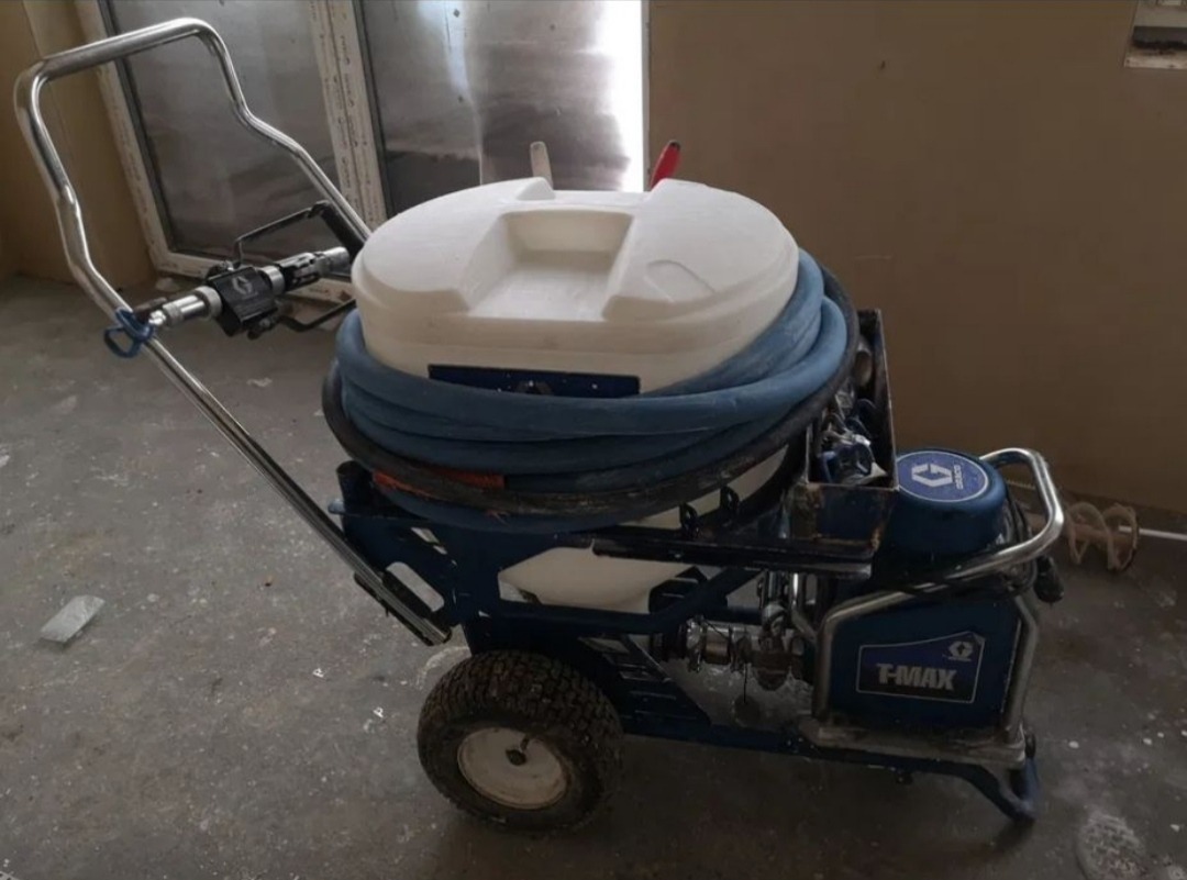 Agregat malarski hydrodynamiczny Graco T-MAX na wózku z niebieskim wężem, gotowy do natrysku szpachli w pomieszczeniu w trakcie prac wykończeniowych.