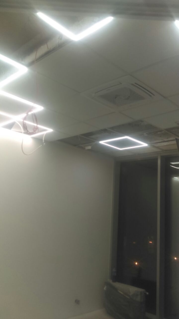 Biuro w trakcie aranżacji: sufit podwieszany z kwadratowymi panelami LED, widoczne przewody i klimatyzacja kasetonowa, ściany przygotowane do malowania, duże okna z widokiem na nocne miasto.