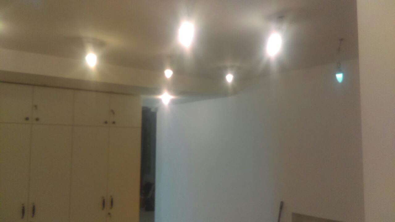 Wnętrze pokoju po odświeżeniu, z jasnymi ścianami, zabudową szaf w kolorze kremowym i nowoczesnym oświetleniem sufitowym.