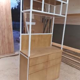 Deco-Stal - Drewniana komoda z sześcioma szufladami i białym metalowym regałem na górze, w surowym otoczeniu warsztatu.