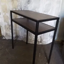 Stolik konsola z dwoma blatami z ciemnego drewna i czarną metalową ramą, na tle wzorzystej tkaniny.