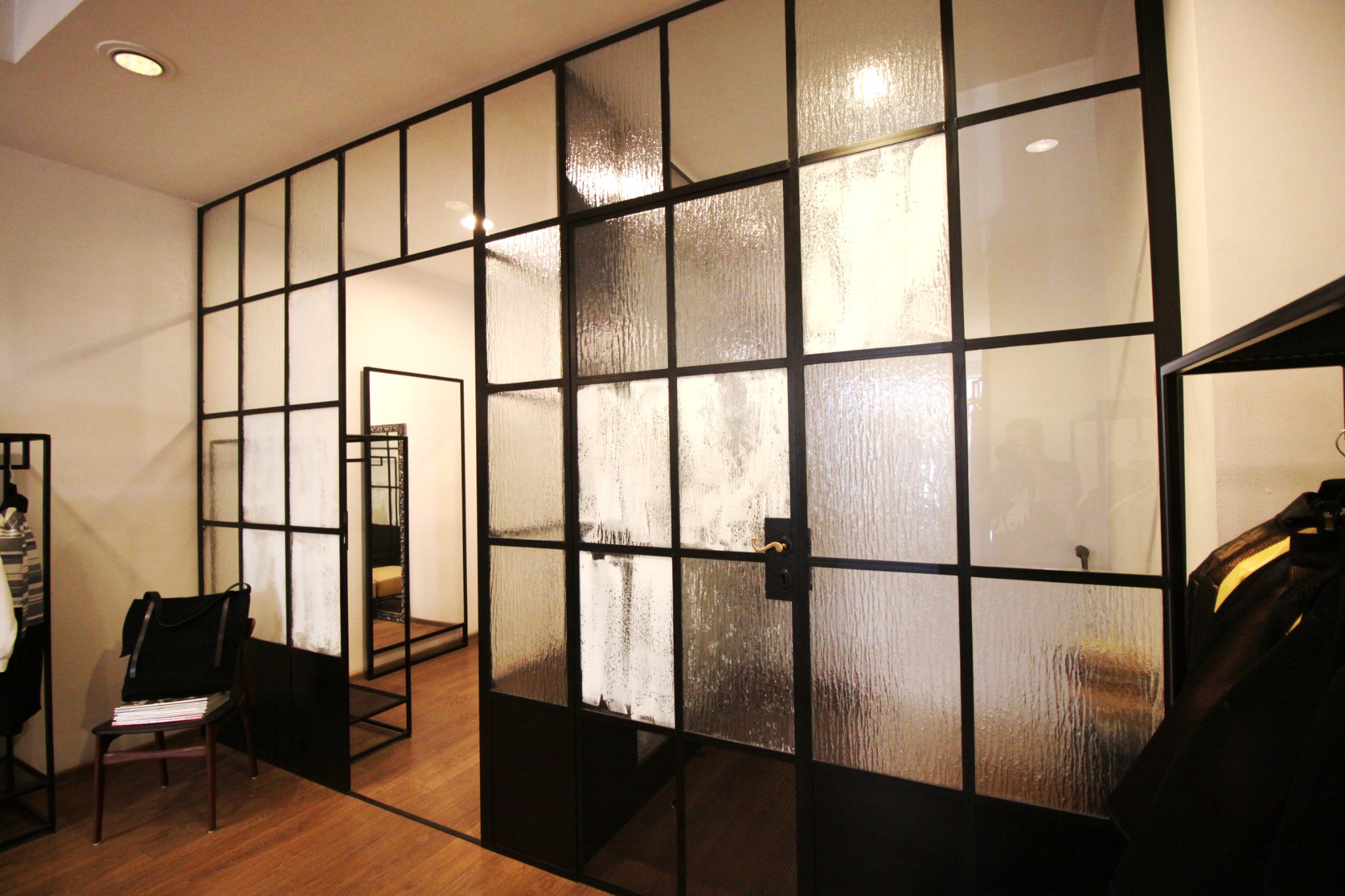 Nowoczesna, przeszklona ścianka działowa z czarnymi profilami, oddzielająca przestrzeń w biurze w Poznaniu. Widoczna faktura szkła i odbicie osoby po drugiej stronie.