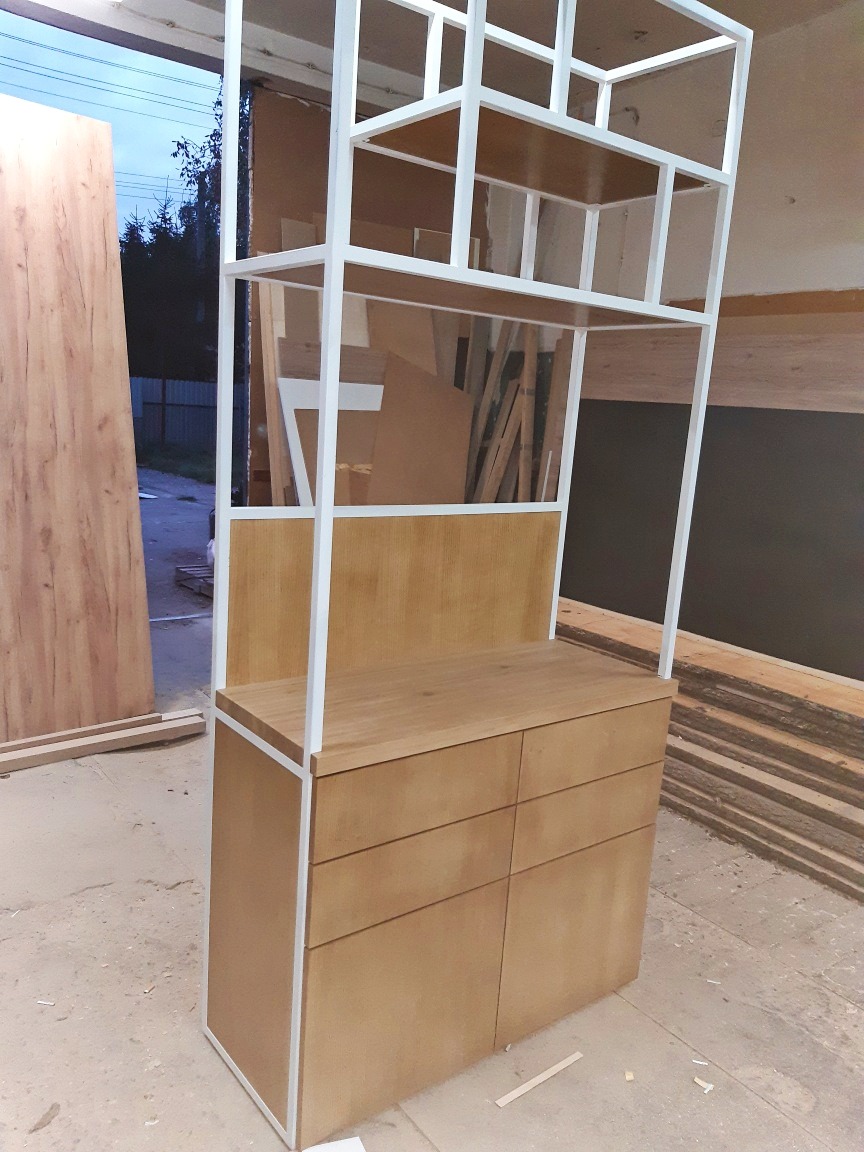 Drewniana komoda z sześcioma szufladami i białym metalowym regałem na górze, w surowym otoczeniu warsztatu.