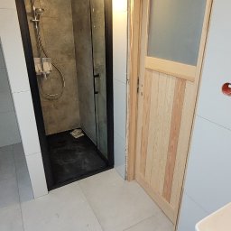 DAMEX-BUD - Wykończona łazienka z kabiną prysznicową typu walk-in z czarną ramą, drewnianą belką stropową i częściowo przeszklonymi, surowymi, drewnianymi drzwiami, płytki podłogowe i ścienne w odcieniach...