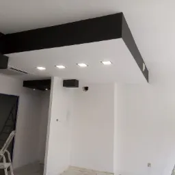 Nowoczesny sufit podwieszany z czarnymi elementami i wpuszczonym oświetleniem w trakcie montażu w Rybniku, widoczne drabiny malarskie.