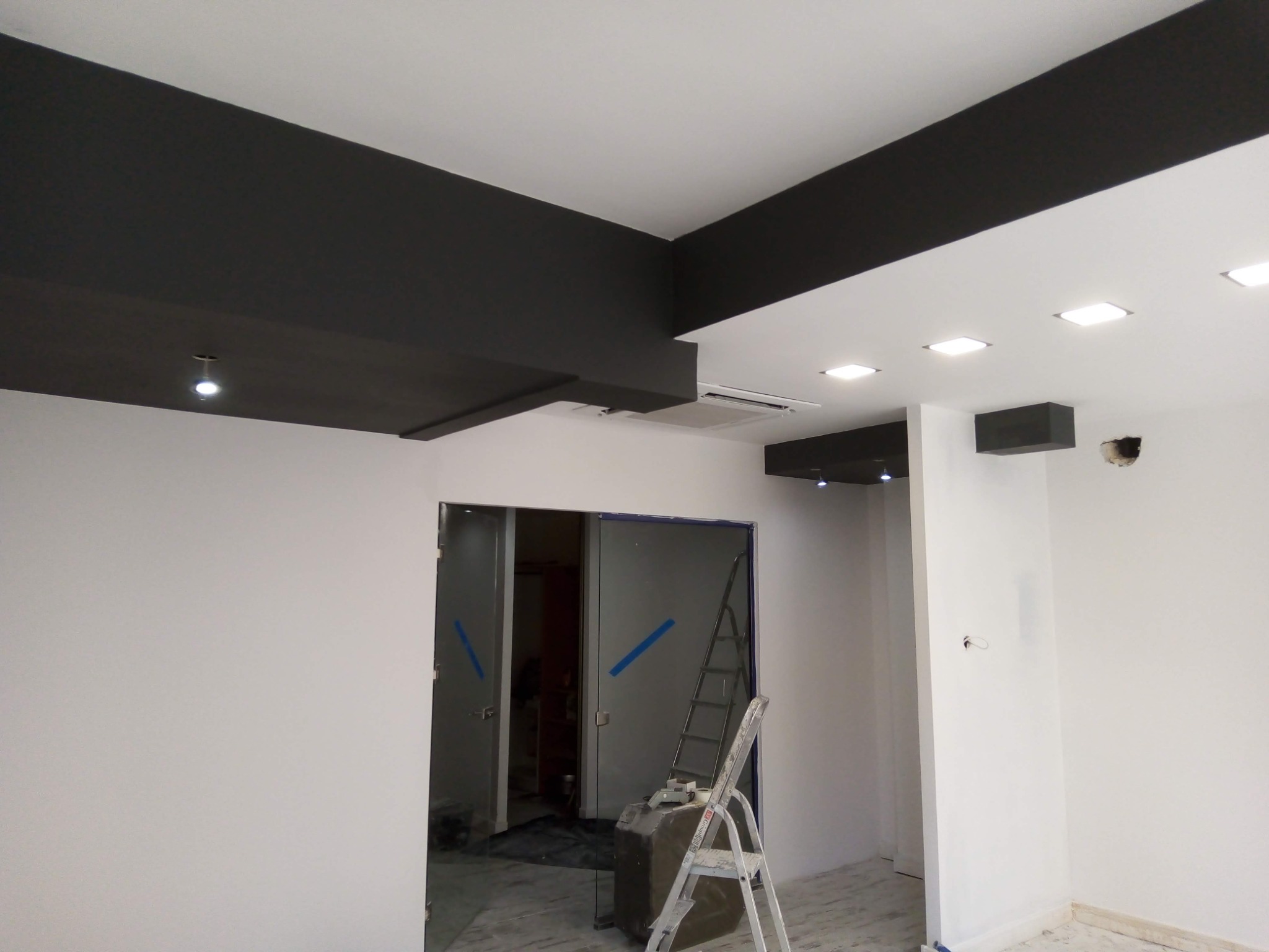 Nowoczesne wnętrze z czarnymi elementami sufitu podwieszanego, białymi ścianami i szklanymi drzwiami przesuwnymi z drabinką opartą o nie.