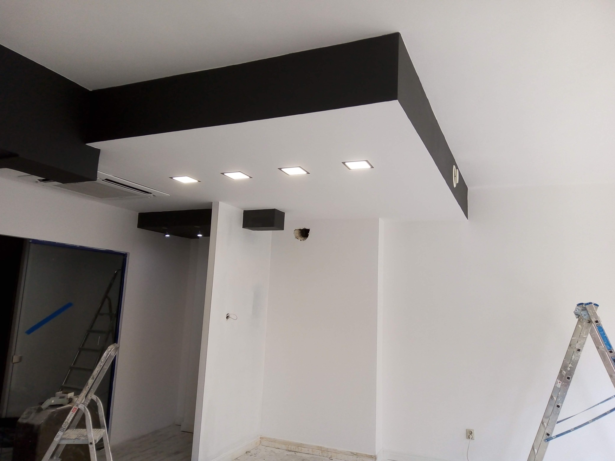 Nowoczesny sufit podwieszany z czarnymi elementami i wpuszczonym oświetleniem w trakcie montażu w Rybniku, widoczne drabiny malarskie.