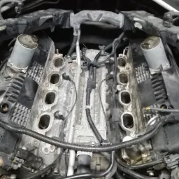 Widok z góry na silnik samochodowy bez kolektora dolotowego, widoczne gniazda wtryskiwaczy, przewody i elementy osprzętu.