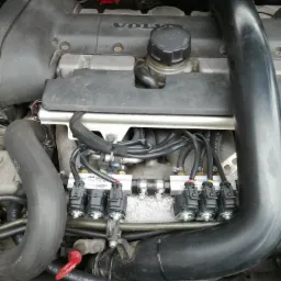 Silnik samochodu z zamontowaną instalacją LPG, widoczny reduktor gazu w kolorze czerwonym, wtryskiwacze gazowe i przewody instalacji.