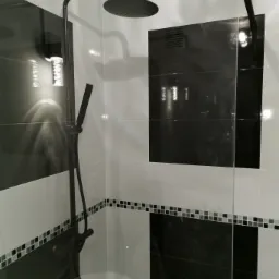 Nowoczesna kabina prysznicowa z czarno-białymi płytkami, deszczownicą i baterią w kolorze czarnym matowym, wykończona mozaiką.