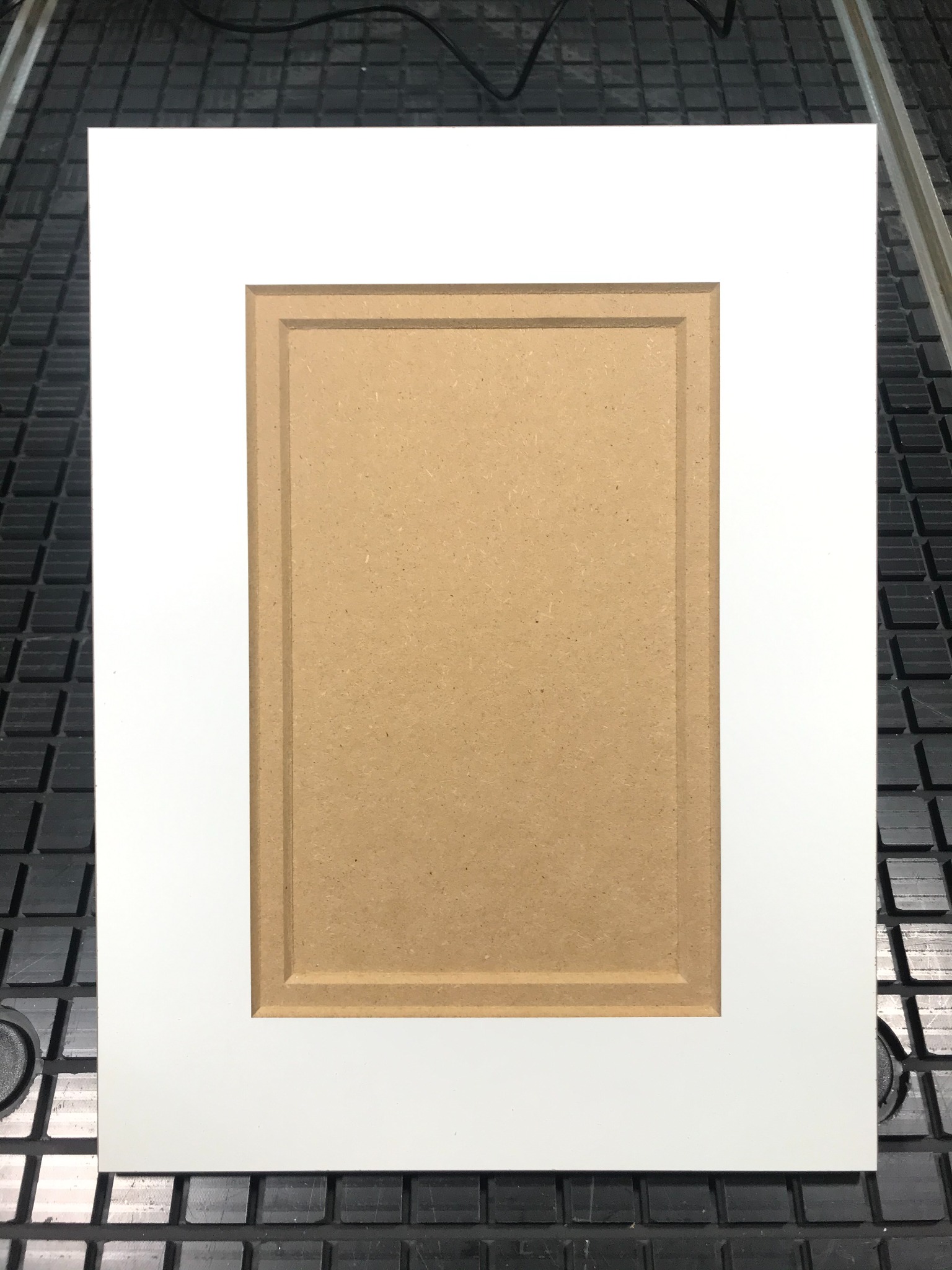 Surowy front meblowy z MDF z frezowanym obramowaniem, leżący na stole roboczym z rastrem.