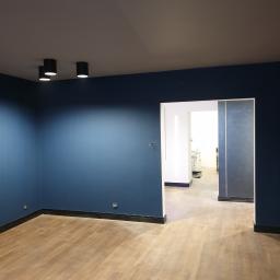 Paweł kudli - Wnętrze po remoncie: ściany pomalowane na ciemny niebieski kolor, drewniana podłoga, czarne listwy przypodłogowe, sufit w kolorze szarym, oświetlenie punktowe, widoczne gniazdka elektryczne...