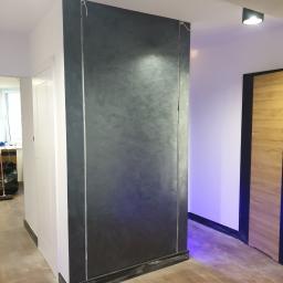 Paweł kudli - Ściana w stylu loft, wykończona szarą, metalizującą farbą dekoracyjną, z widocznymi pionowymi paskami imitującymi metalowe profile, w nowoczesnym wnętrzu z drewnianą podłogą i drzwiami.