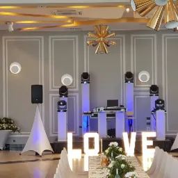 Sala bankietowa z profesjonalnym nagłośnieniem i oświetleniem scenicznym, dekoracją LOVE z kwiatami na pierwszym planie, przygotowana na imprezę okolicznościową.