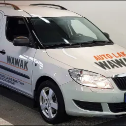 Jasny samochód dostawczy z pomarańczowo-czarną grafiką reklamową firmy Auto-Lak Wawak, specjalizującej się w blacharstwie i lakiernictwie samochodowym, zaparkowany w hali.