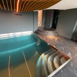 MAX HOME GLAZURNICTWO Szymon Pomarański - Nowoczesny basen w pomieszczeniu z marmurową posadzką i schodami. Oświetlenie LED podkreśla drewniany sufit i turkusową wodę. Minimalistyczny design.