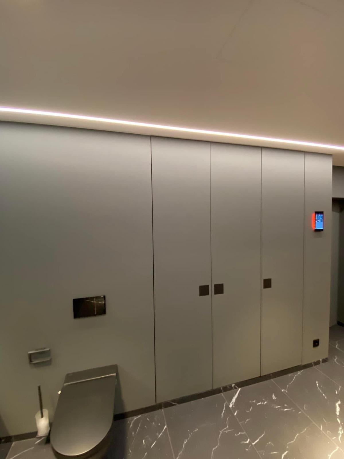 Nowoczesna łazienka w szarościach: zabudowa meblowa pod sufit z podświetleniem LED, wisząca toaleta i marmurowe płytki podłogowe. Minimalistyczny design.