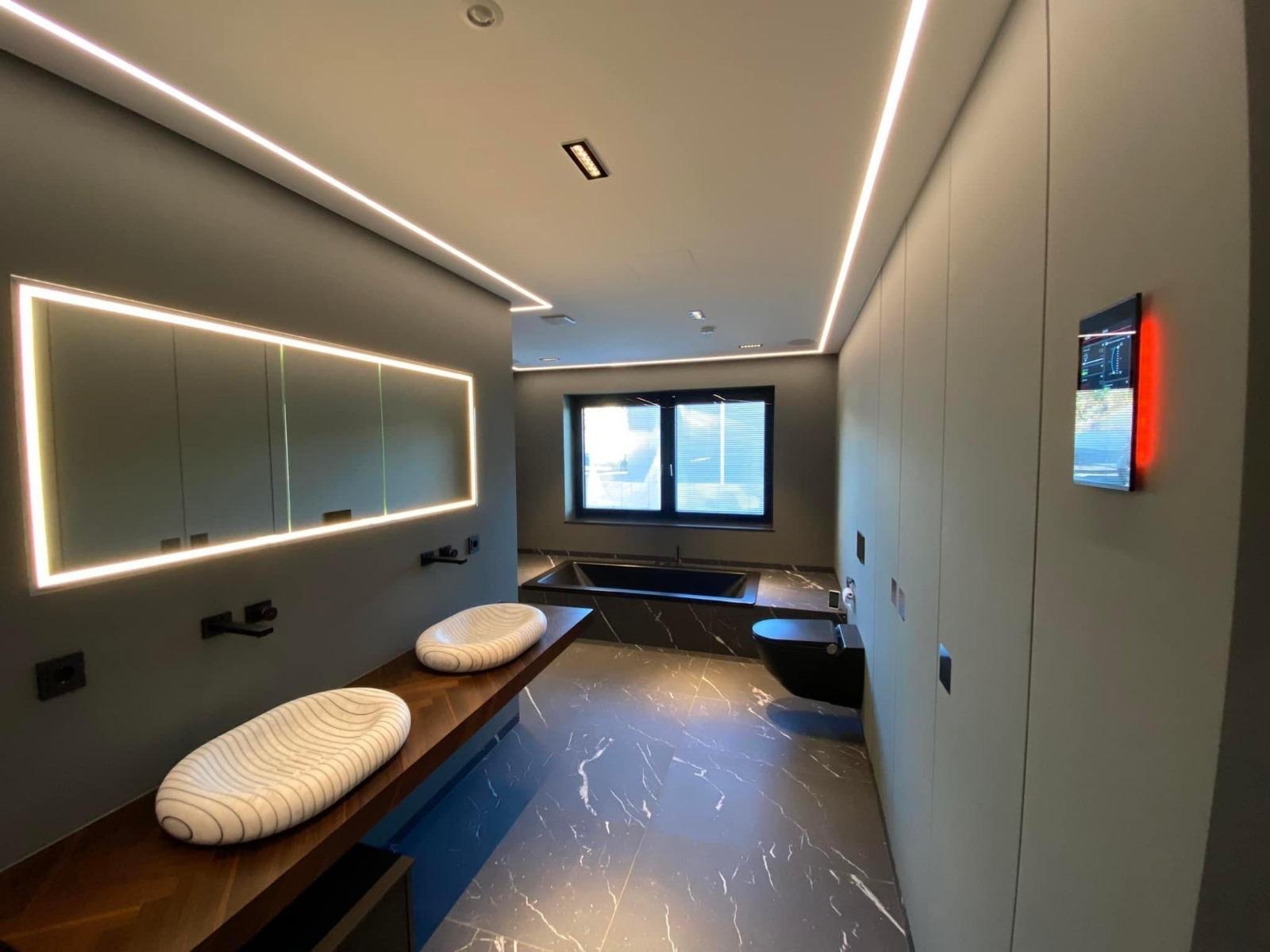 Nowoczesna łazienka z podświetlanym lustrem, marmurową podłogą i designerskimi umywalkami. Minimalistyczny styl, stonowana kolorystyka, oświetlenie LED.