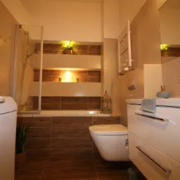 Nowoczesna łazienka z wanną obudowaną brązowymi płytkami, podświetlanymi wnękami, białą umywalką z chromowaną baterią i pralką z boku.