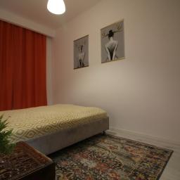 SILFOX nieruchomości Sebastian Lis - Pokój z łóżkiem, pomarańczowymi zasłonami, dywanem w stylu vintage i dwoma obrazami z motywem kobiety z porożem jelenia na ścianie.