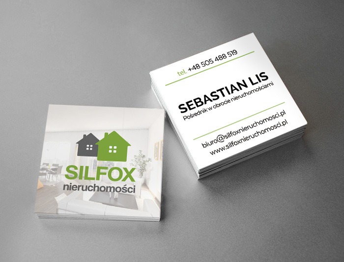 Wizytówki firmy Silfox nieruchomości, z logo przedstawiającym dwa domy (szary i zielony) na tle wnętrza mieszkania, obok stos wizytówek z danymi kontaktowymi pośrednika Sebastiana Lisa.