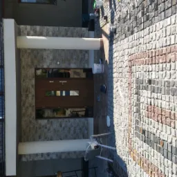 Elewacja domu z kamienia naturalnego z drewnianymi drzwiami i oknem z kwiatami, oraz wybrukowany chodnik z kostki granitowej w odcieniach szarości i różu.