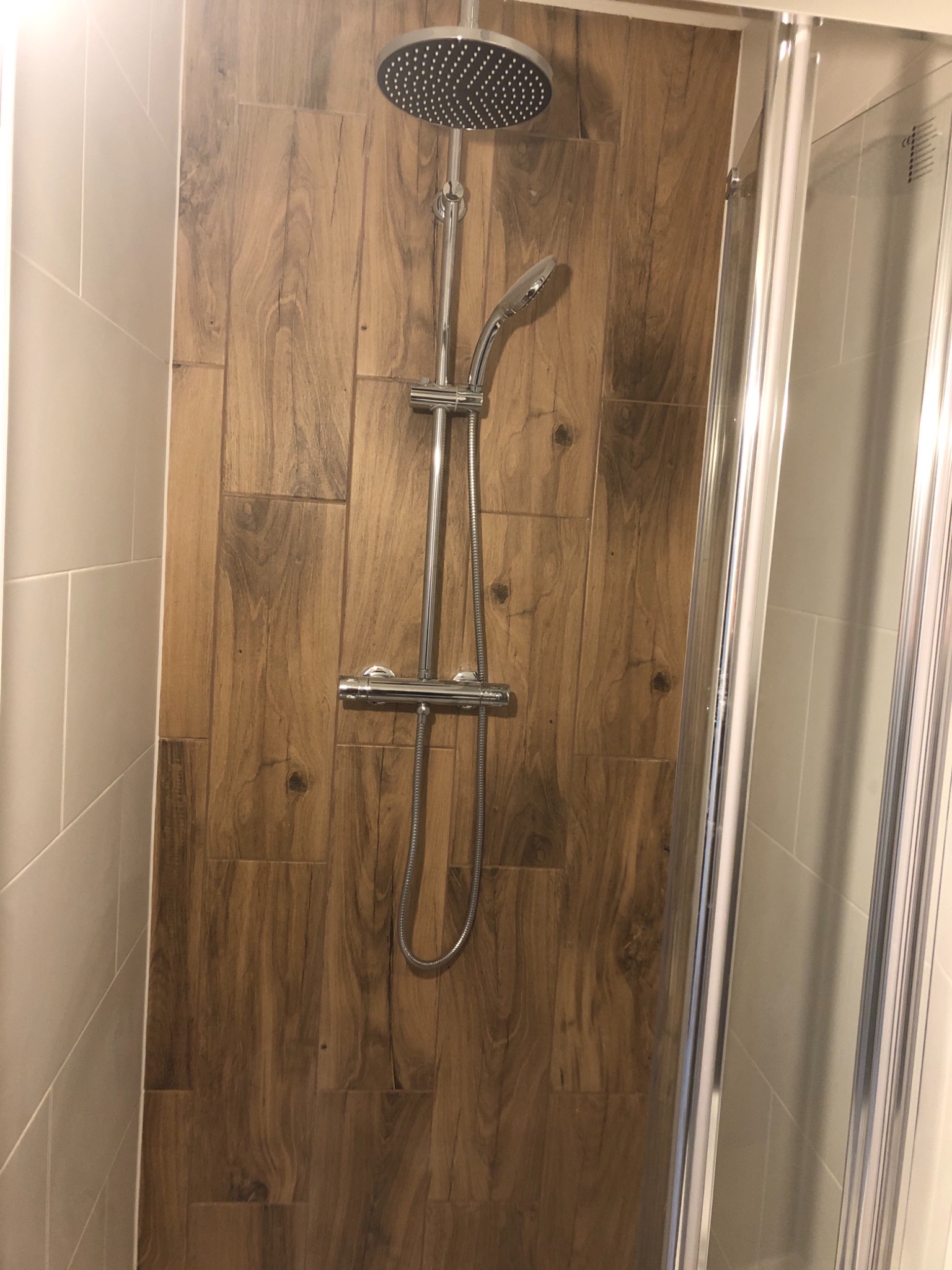 Kabinę prysznicową wyłożono płytkami imitującymi drewno, z zamontowaną chromowaną armaturą i deszczownicą.