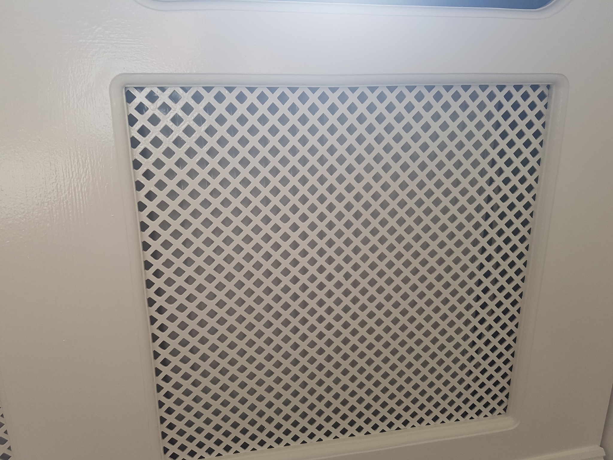 Biały, pomalowany grzejnik z ozdobną kratką w obudowie, widok z bliska.