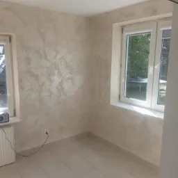 Pokój po malowaniu ścian z efektem dekoracyjnym, jasne płytki na podłodze, białe okna, grzejnik pod oknem po lewej.