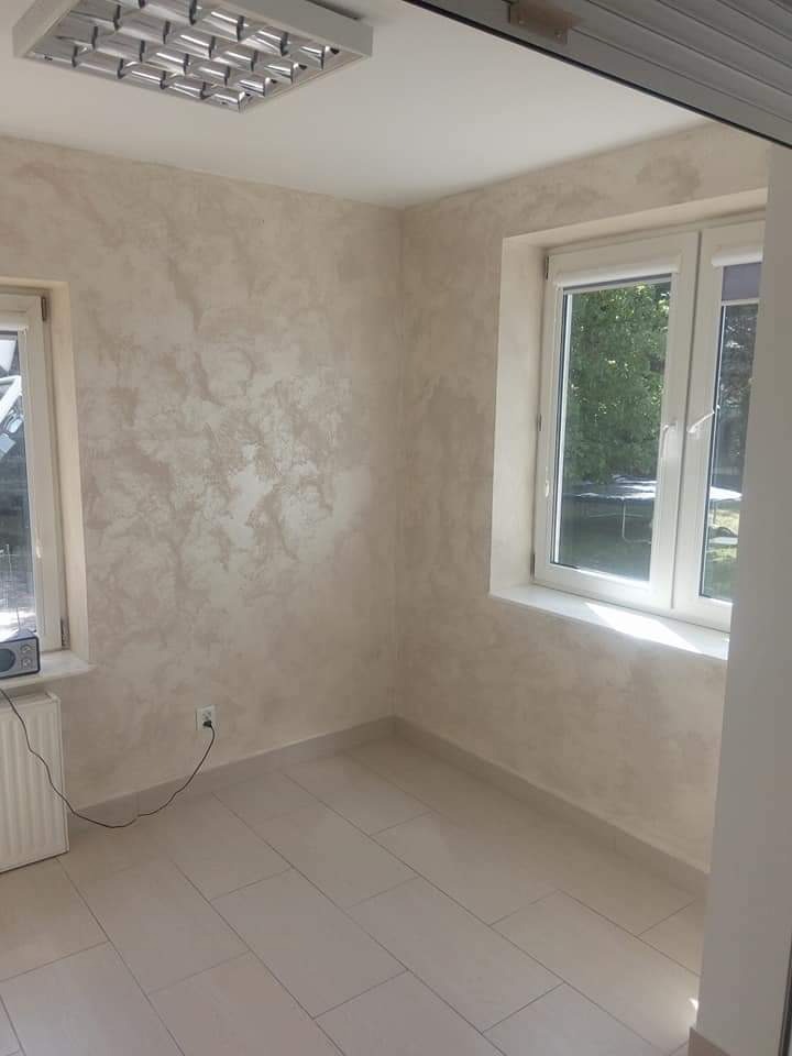 Pokój po malowaniu ścian z efektem dekoracyjnym, jasne płytki na podłodze, białe okna, grzejnik pod oknem po lewej.