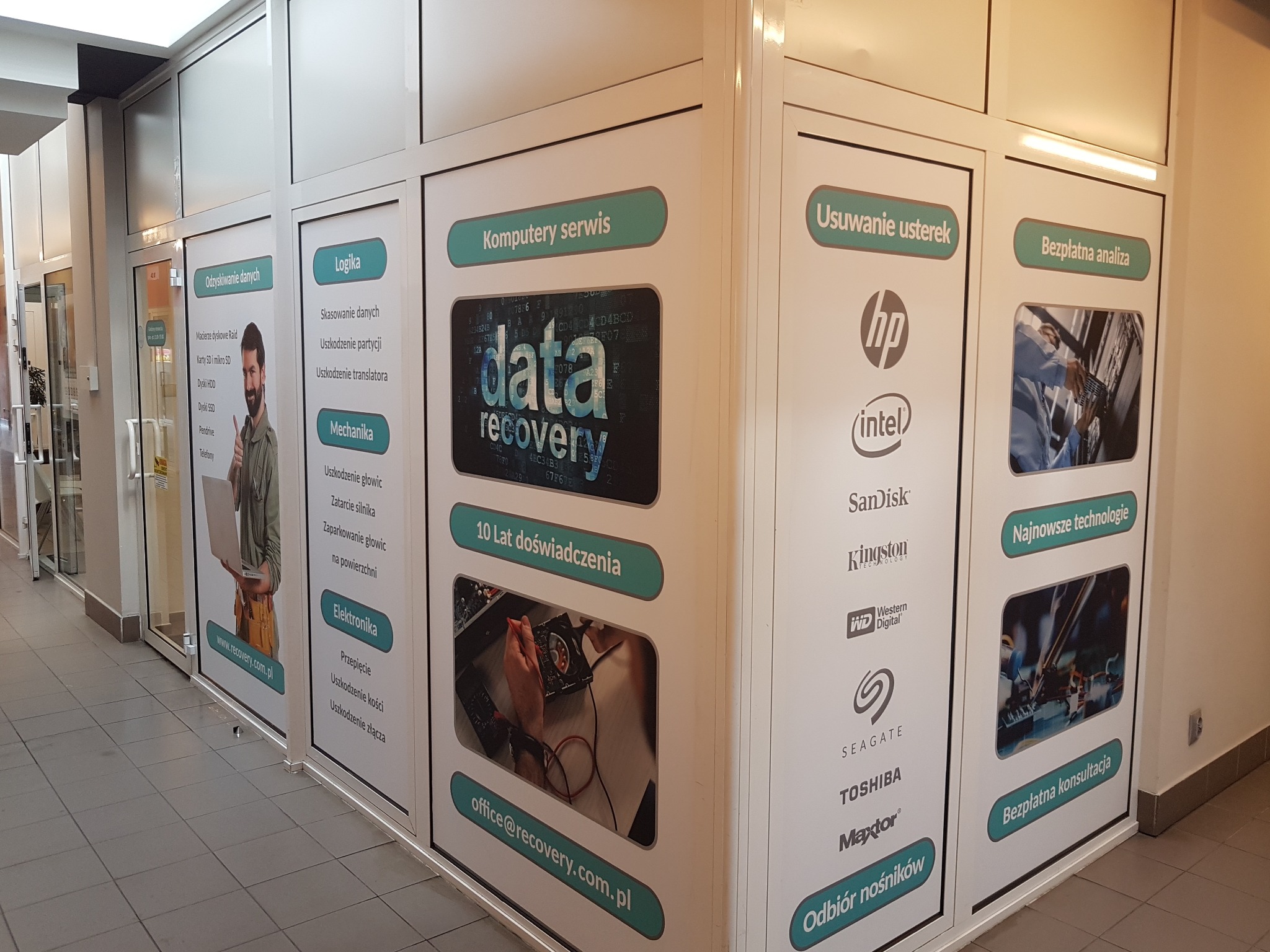 Reklama usług firmy informatycznej: plansze z ofertą naprawy komputerów i odzyskiwania danych, logotypy producentów podzespołów, hasła reklamowe i adres e-mail.