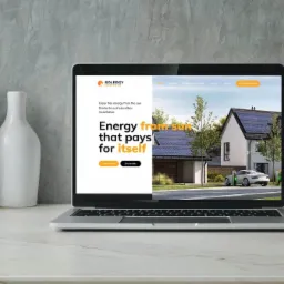 Laptop wyświetla stronę internetową firmy oferującej panele słoneczne, z widocznym domem z panelami i ładującym się samochodem elektrycznym, na tle dekoracyjnej ściany i wazonów.