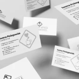 Białe wizytówki z logo Coffee Style, ułożone pod kątem na szarym tle, prezentujące dane kontaktowe Iwony Pożegowiak, profesjonalnej obsługi baristycznej wesel, targów i eventów.