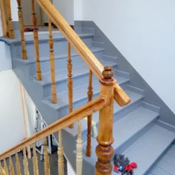 Odnowione schody drewniane z jasną balustradą i szarymi stopniami. Na jednym ze stopni leżą robocze rękawice.