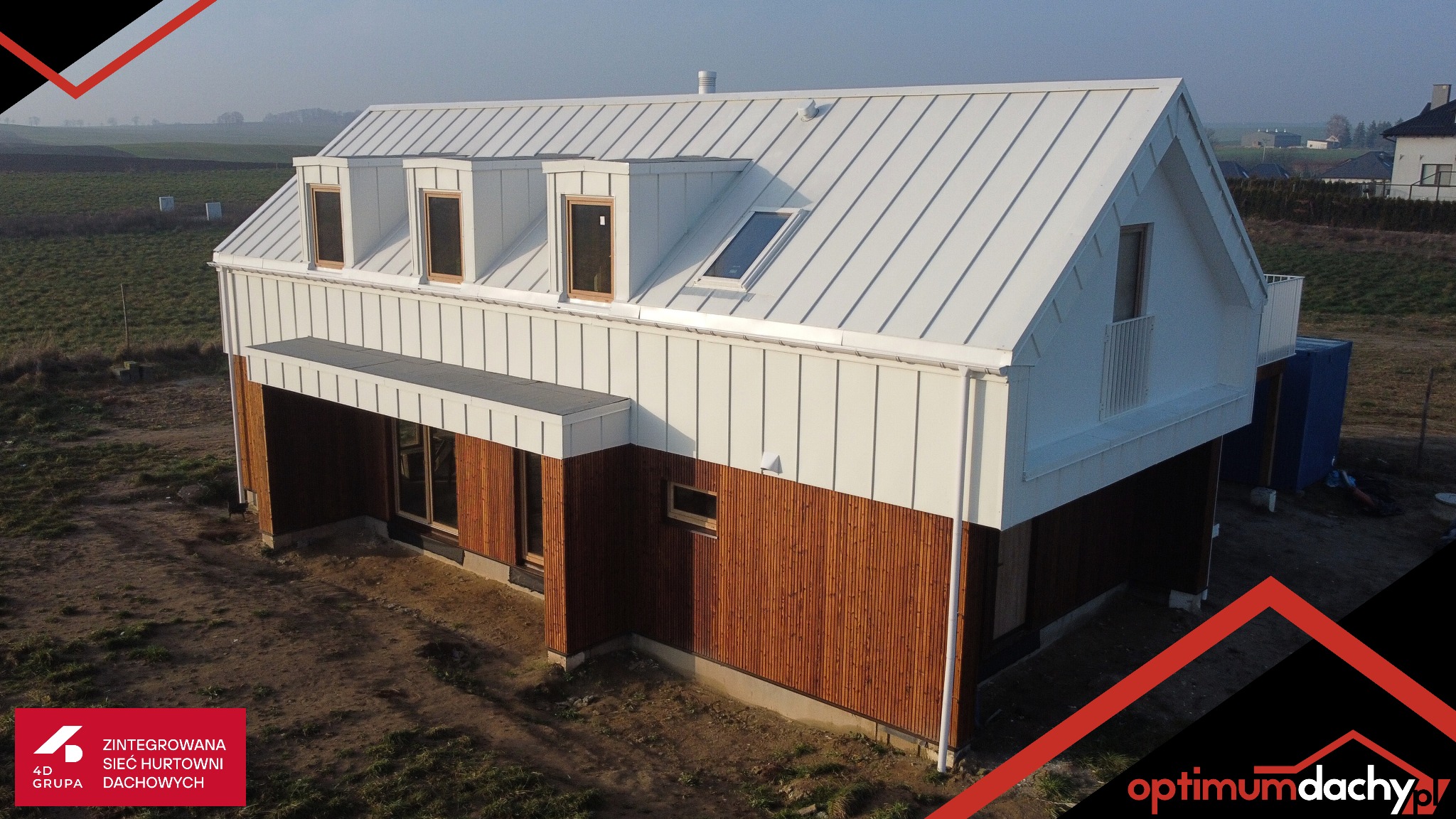 Nowoczesny dom z białym dachem z blachy na rąbek stojący i drewnianą elewacją, widok z góry, w tle pola i zabudowa.