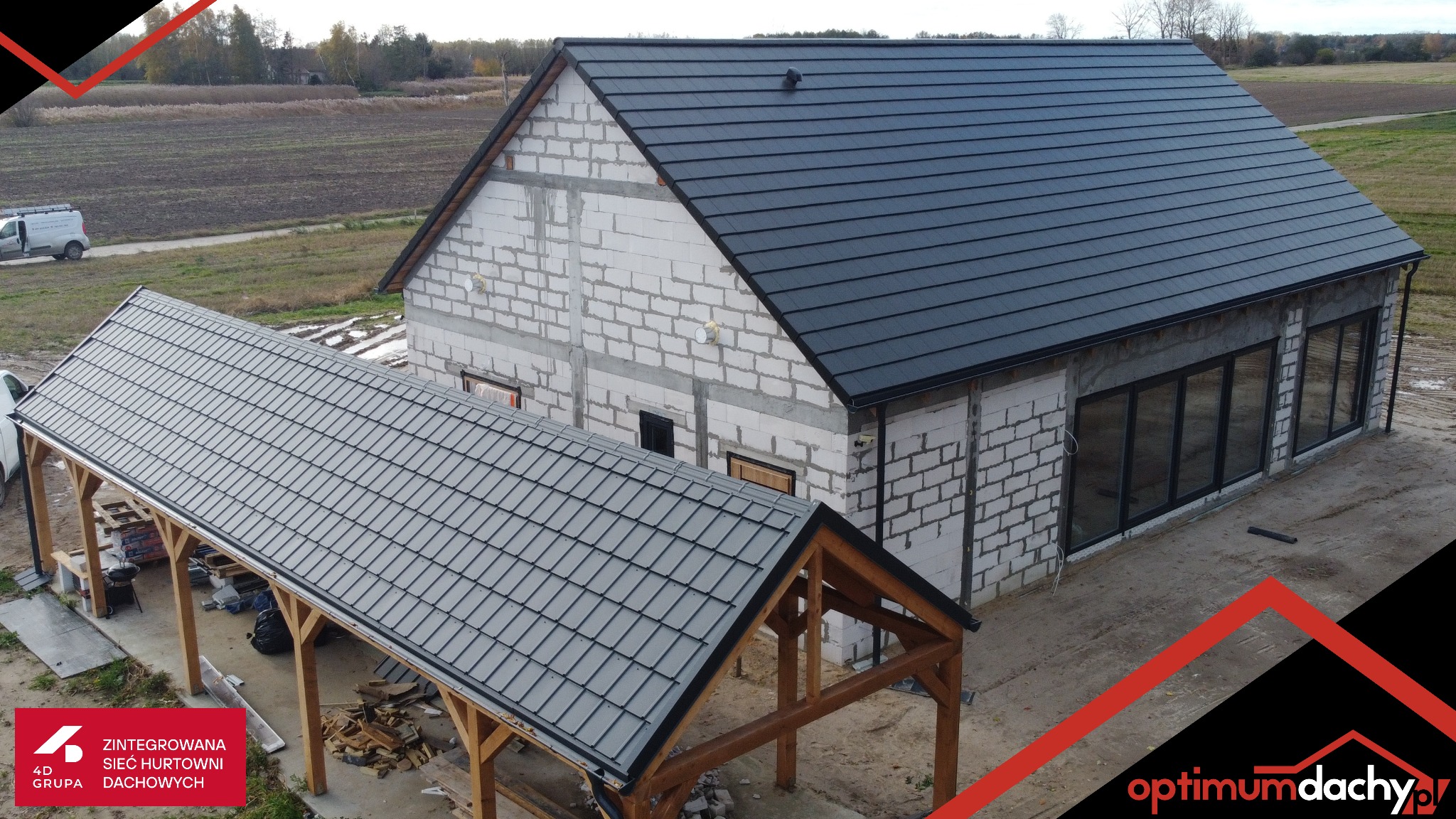 Nowoczesny dom w trakcie budowy z ciemnoszarą dachówką ceramiczną i zadaszeniem tarasu o identycznym pokryciu. Widoczny surowy stan ścian z betonu komórkowego.