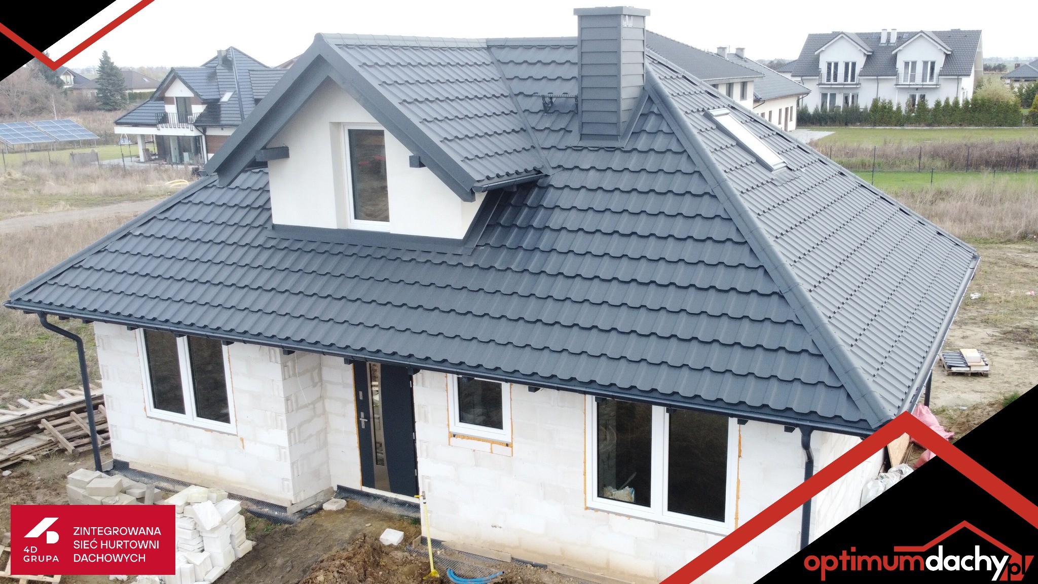 Dom jednorodzinny w trakcie budowy z ciemnoszarym dachem z dachówki modułowej i orynnowaniem. Widoczne okna dachowe i komin.