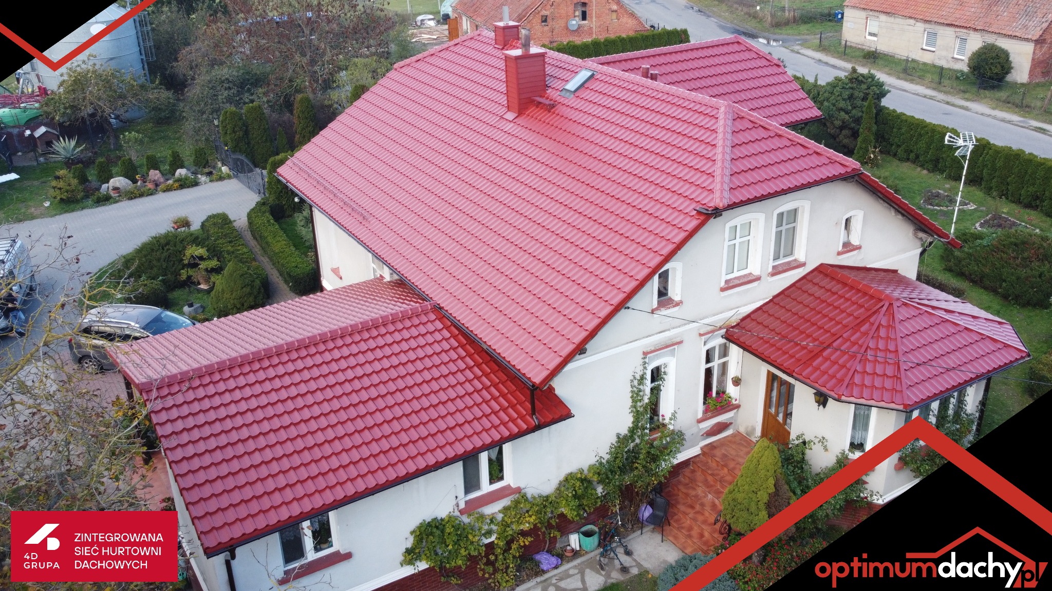 Dom z nowym, czerwonym dachem z dachówki, widok z góry. Charakterystyczny komin i okno dachowe. Otoczenie domu: ogród i droga.