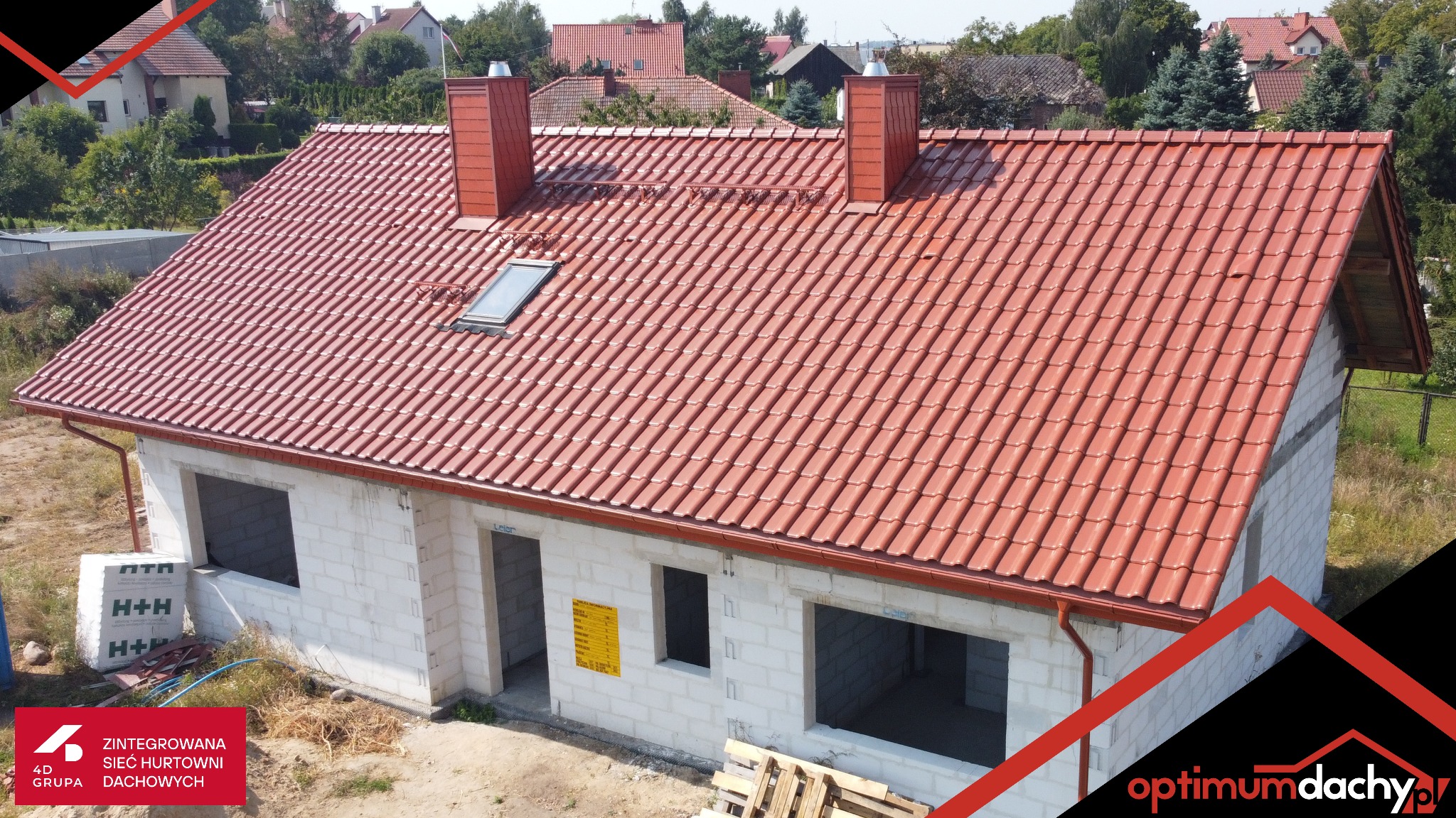 Czerwony dach z dachówki ceramicznej na surowym budynku z białego bloczka, widoczne kominy i rynny w tym samym kolorze, okno dachowe.