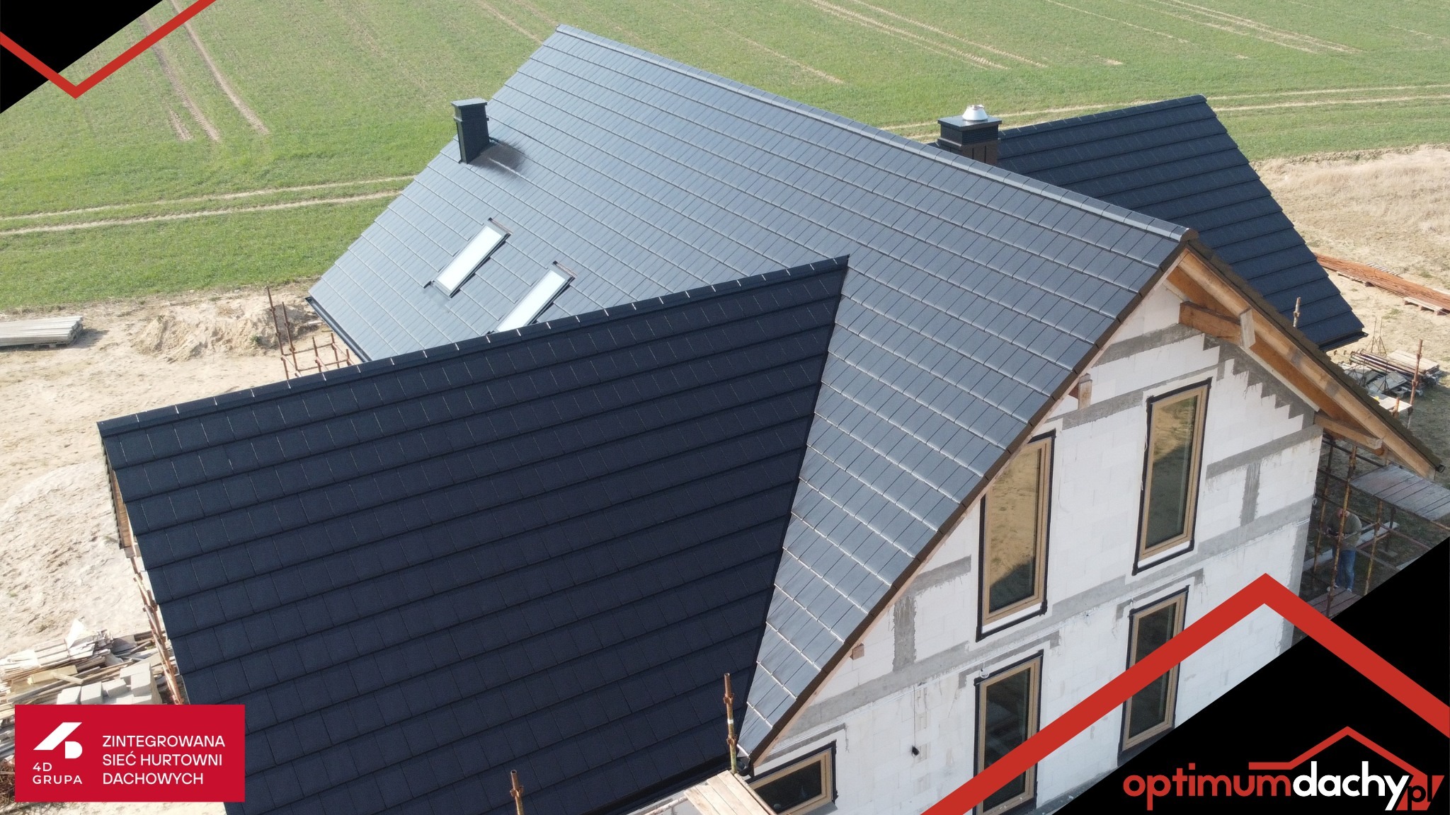 Nowoczesny dom w trakcie budowy z ciemnoszarą dachówką ceramiczną, widok z góry, okna dachowe, częściowo otynkowana elewacja, zielone pole w tle.