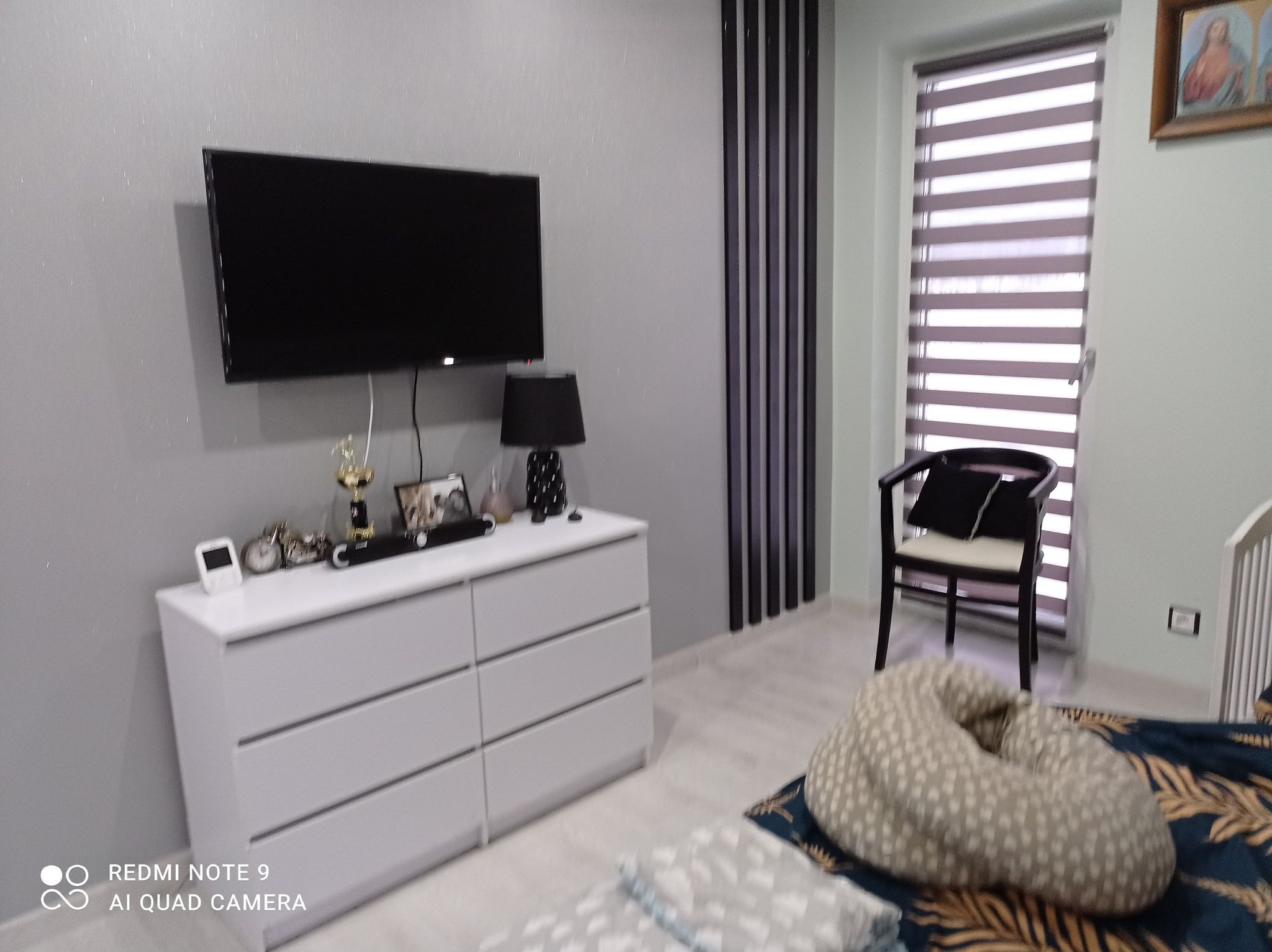 Szary pokój z białymi meblami, czarnym telewizorem i roletami okiennymi typu dzień-noc.