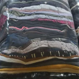 Duży pakiet sprasowanych, używanych ubrań w przezroczystej folii, z widocznymi warstwami różnych tkanin i kolorów, ułożonych jeden na drugim.