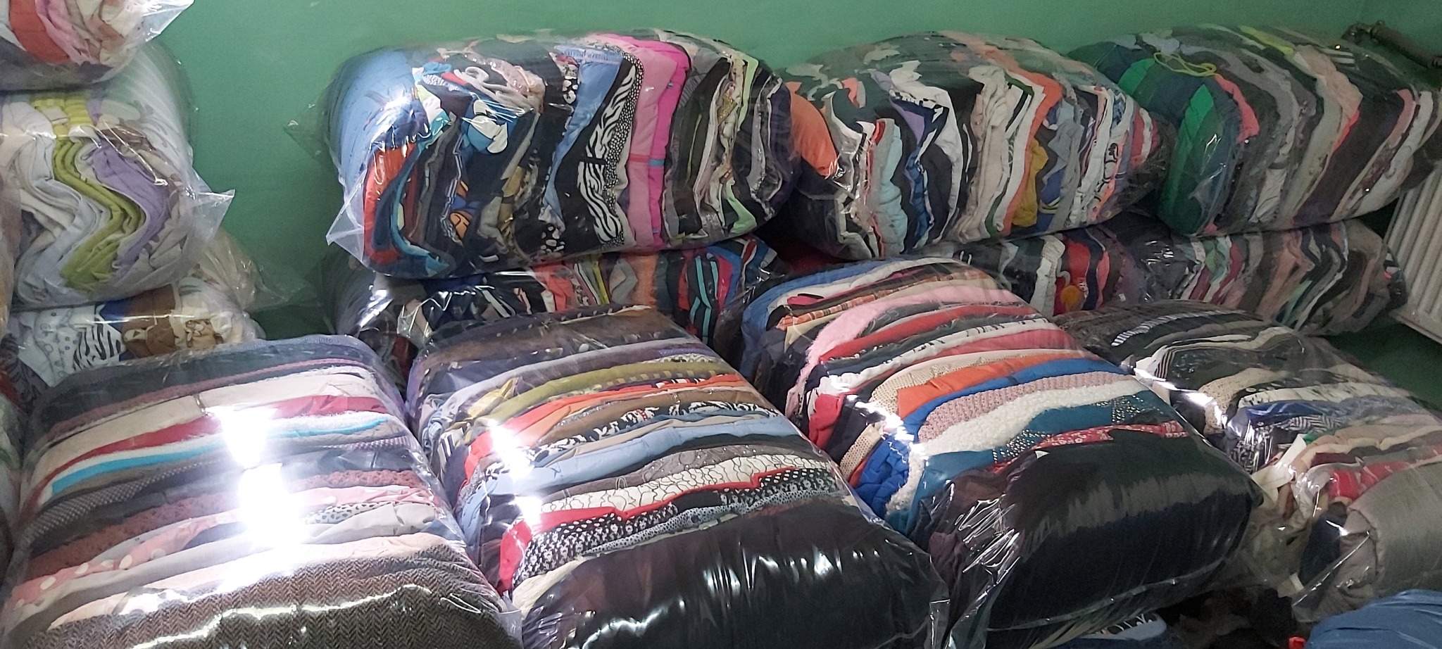 Stosy sprasowanej odzieży w przezroczystych foliowych workach, widoczne warstwy różnorodnych ubrań, odzież ułożona w regularne pakiety.