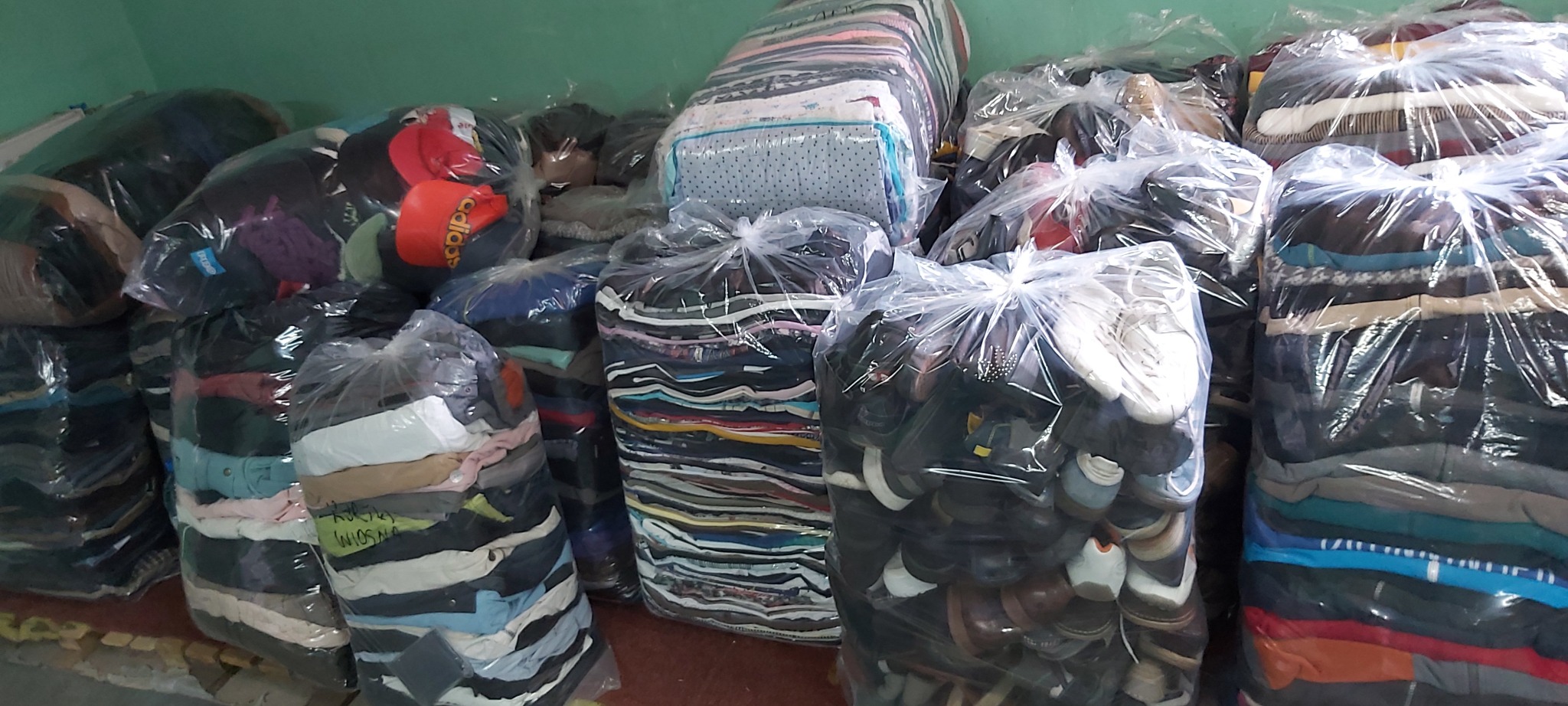 Spakowane w przezroczyste worki paki z odzieżą używaną i obuwiem, przygotowane do transportu w Szczecinie. Na pierwszym planie worek z obuwiem, w tle paki z odzieżą.