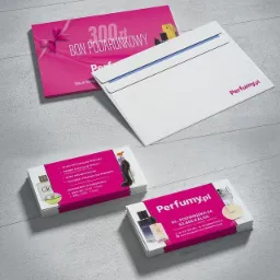 Zestaw materiałów reklamowych perfumerii: wizytówki z logo i adresem, bon podarunkowy z kwotą 300 zł oraz biała koperta z logo firmy na szarym tle.