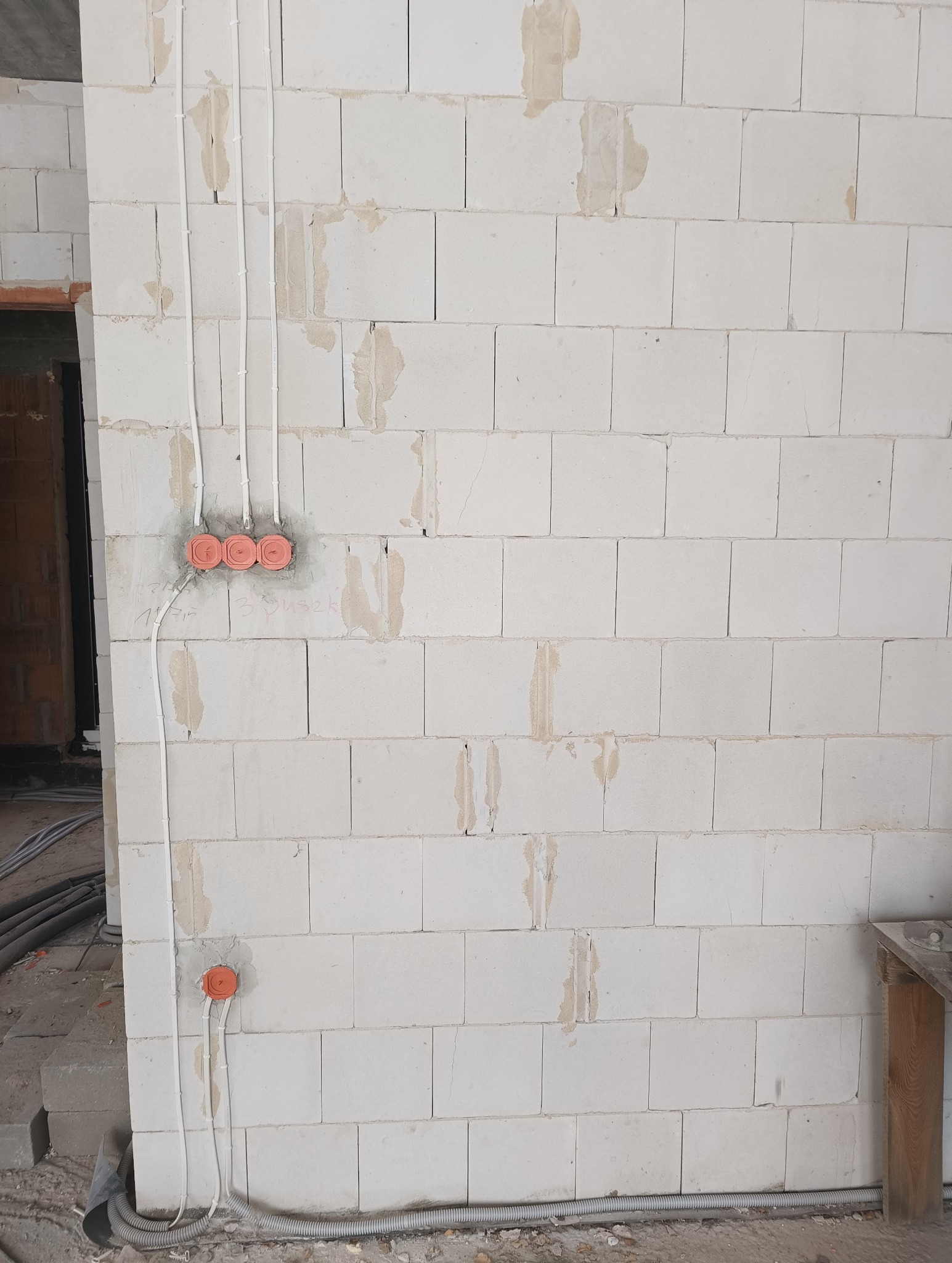 Ściana z betonu komórkowego z widocznymi przewodami elektrycznymi w białych rurkach i pomarańczowymi puszkami pod gniazdka, w trakcie montażu instalacji.