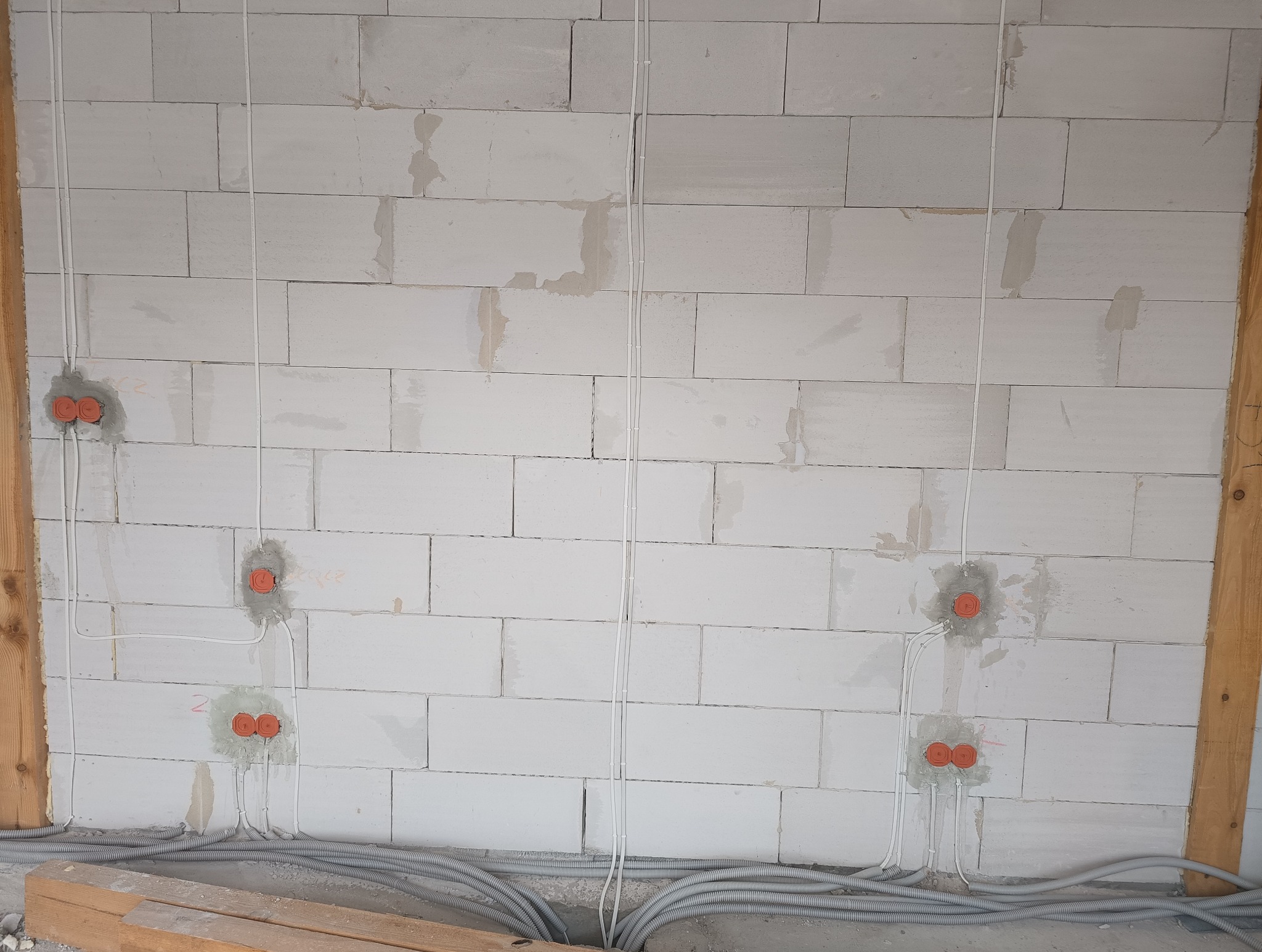 Ściana z betonu komórkowego z widocznymi puszkami instalacyjnymi i przewodami elektrycznymi, częściowo zamurowana. Przewody prowadzone wzdłuż ściany, układane w korytach pod podłogą.