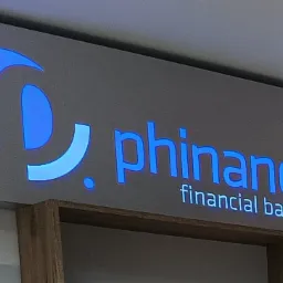 Podświetlany szyld firmy 'phinance financial balance' z niebieskim logo i nazwą, zamontowany na ścianie.