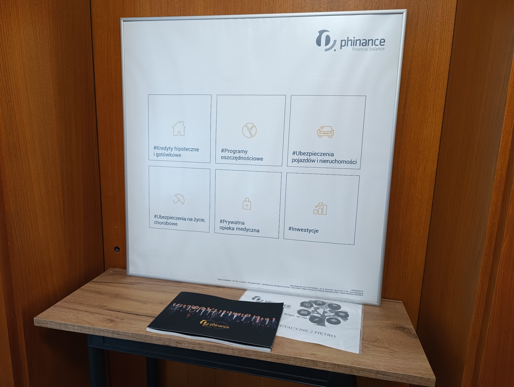 Tablica informacyjna firmy Phinance z ofertą kredytów, programów oszczędnościowych, ubezpieczeń pojazdów i nieruchomości, ubezpieczeń na życie, prywatnej opieki medycznej i inwestycji, leżąca...