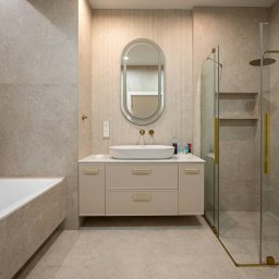 Royal Design Projektowanie Wnętrz Joanna Kowalska - Elegancka łazienka w beżach: owalne lustro z podświetleniem, biała umywalka nablatowa, kabina prysznicowa ze złotymi detalami i wanna.